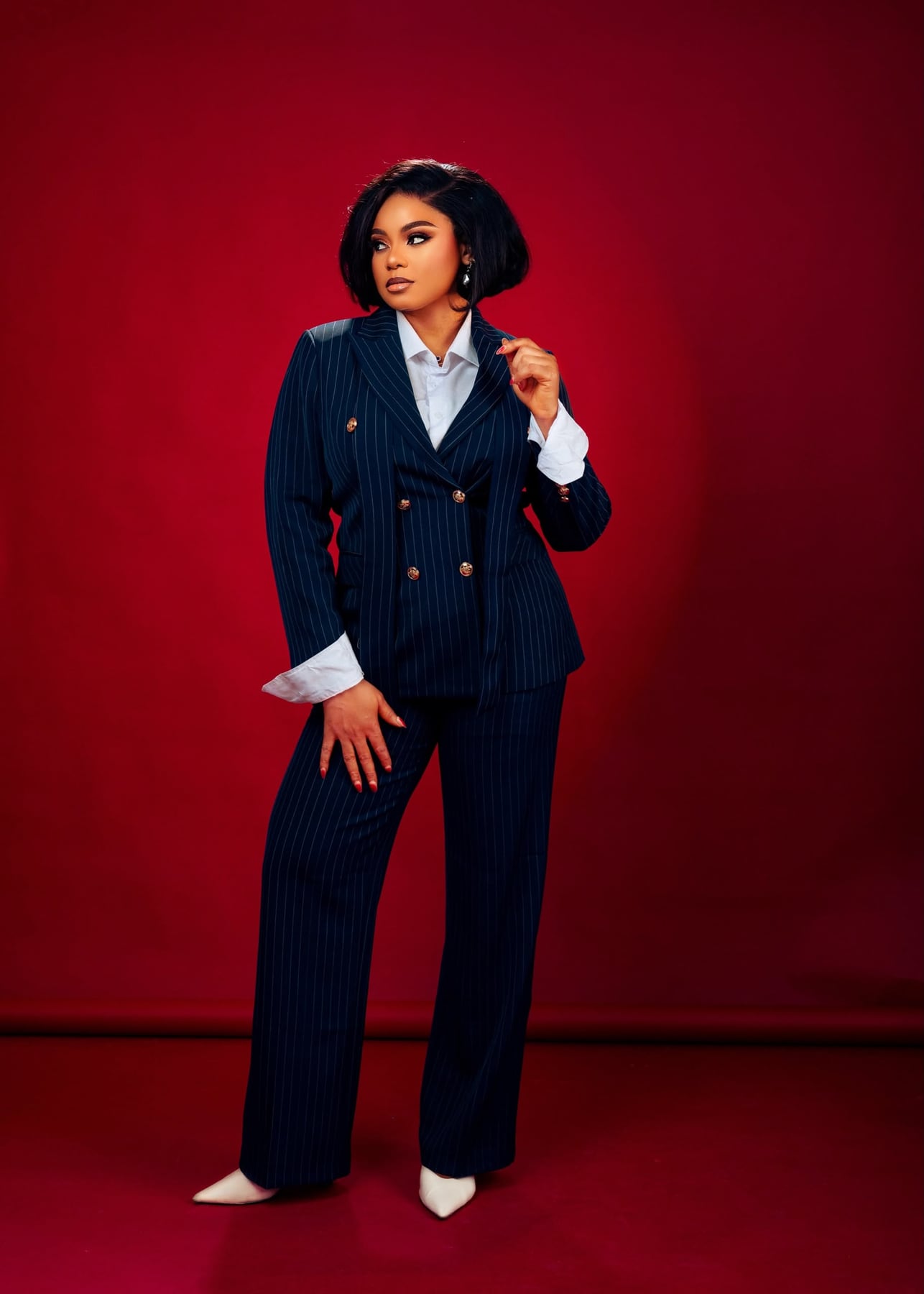 Tessy Kiri Bibowei in a navy pinstripe suit against a deep crimson studio wall